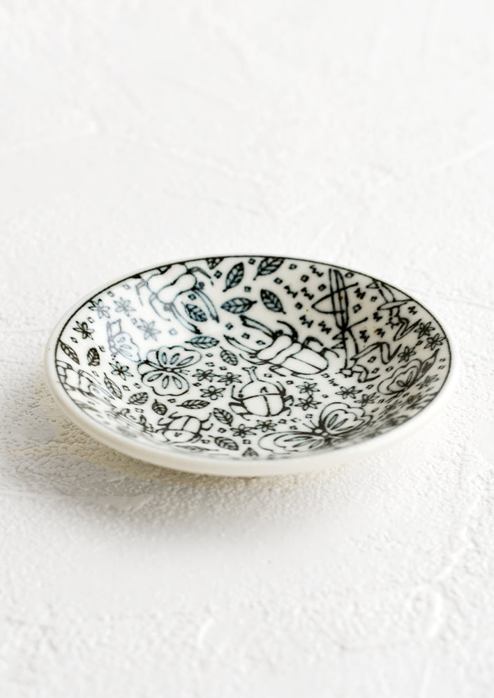 A round ceramic trinket dish in black and white with insect print.
