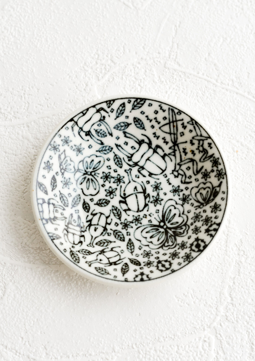 1: A round ceramic trinket dish in black and white with insect print.