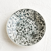 1: A round ceramic trinket dish in black and white with insect print.