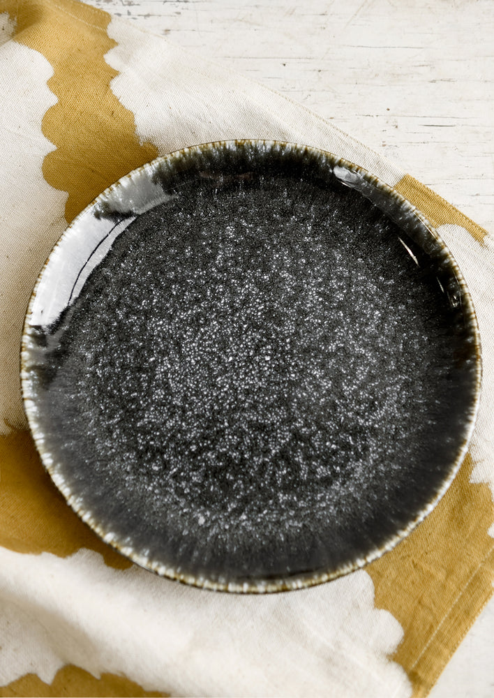 1: A round plate in glossy black speckled glaze.