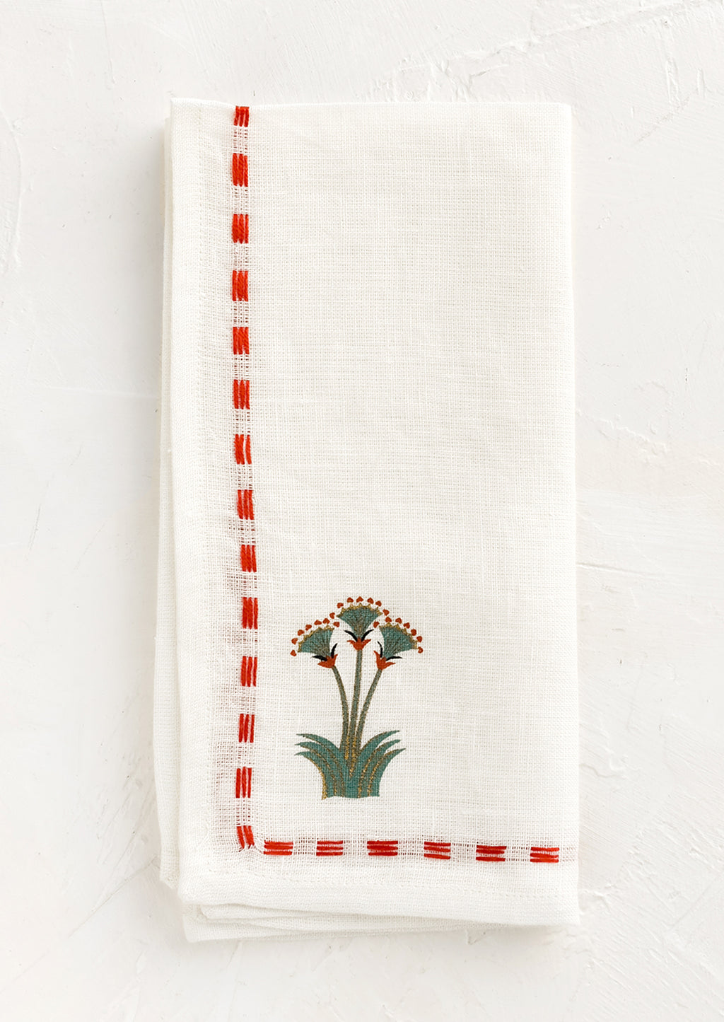 Red Multi: A white linen napkin with stitched red border and nile lotus emblem at corner.