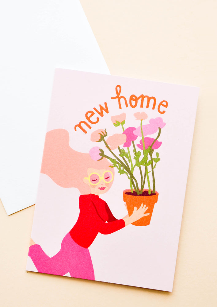 Pink notecard with drawing of girl holding a Flowerpot and the text "New Home", with white envelope.