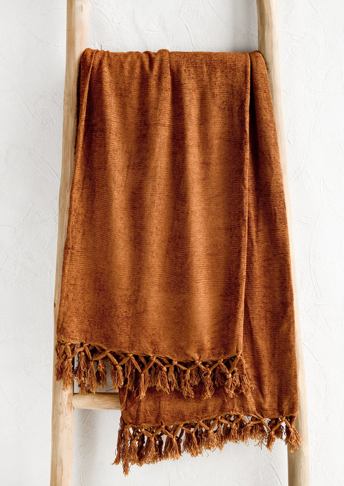 A chenille throw with knotted tassel trim in nutmeg copper color.