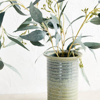 2: A blue-green ceramic vase with eucalyptus.