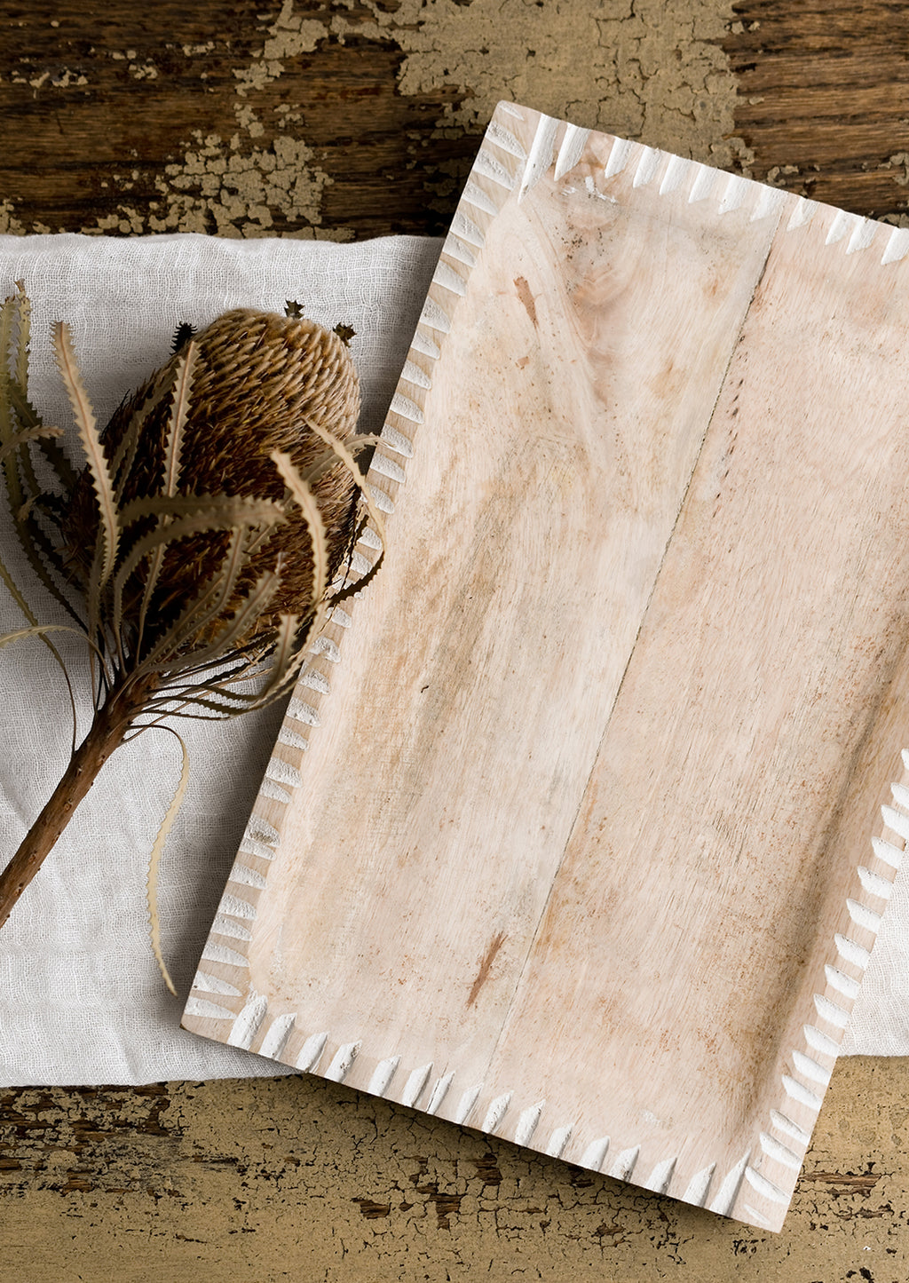 3: A dried protea flower displayed on a wooden tray.