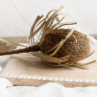 4: A dried protea flower displayed on a wooden tray.