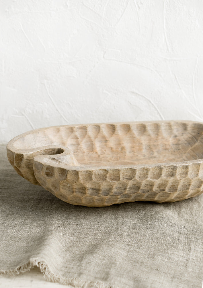 A light wooden bowl in organic, oblong shape, with notched texture.