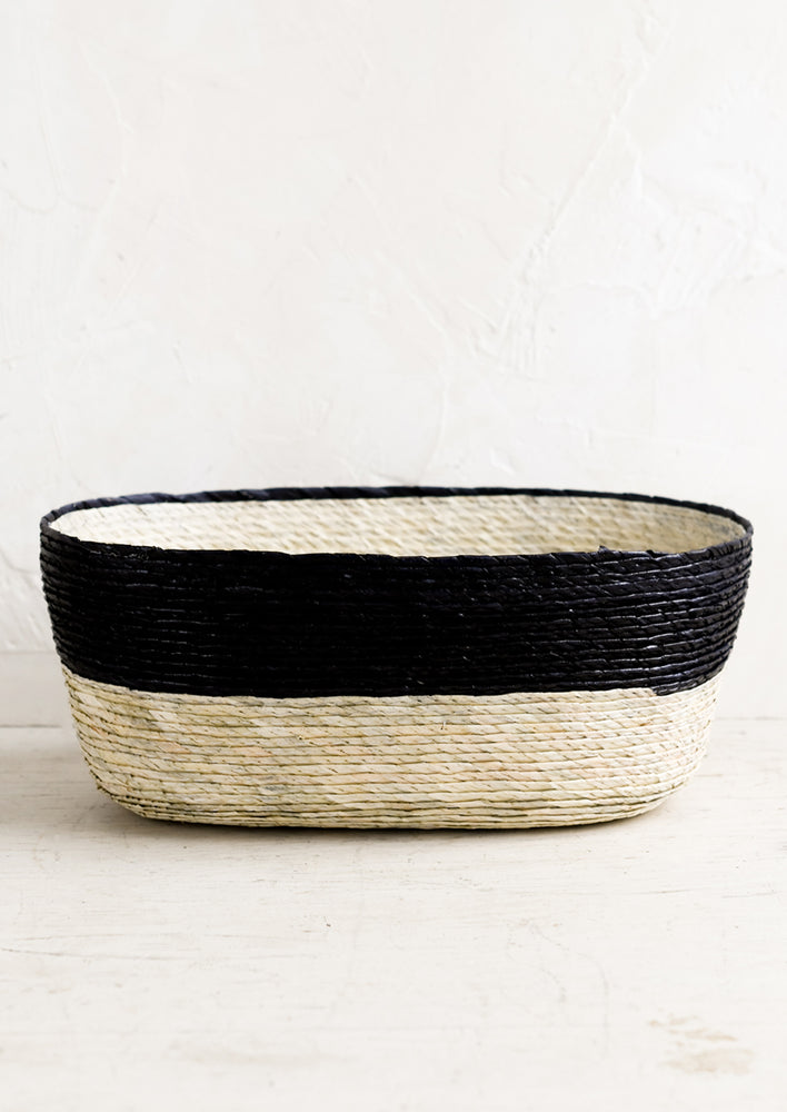 A two-tone oval shaped storage basket in natural and carbon.