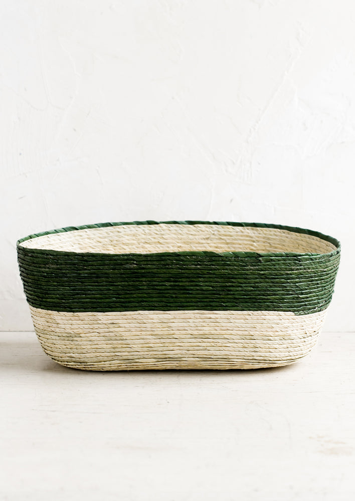 A two-tone oval shaped storage basket in natural and pine green.