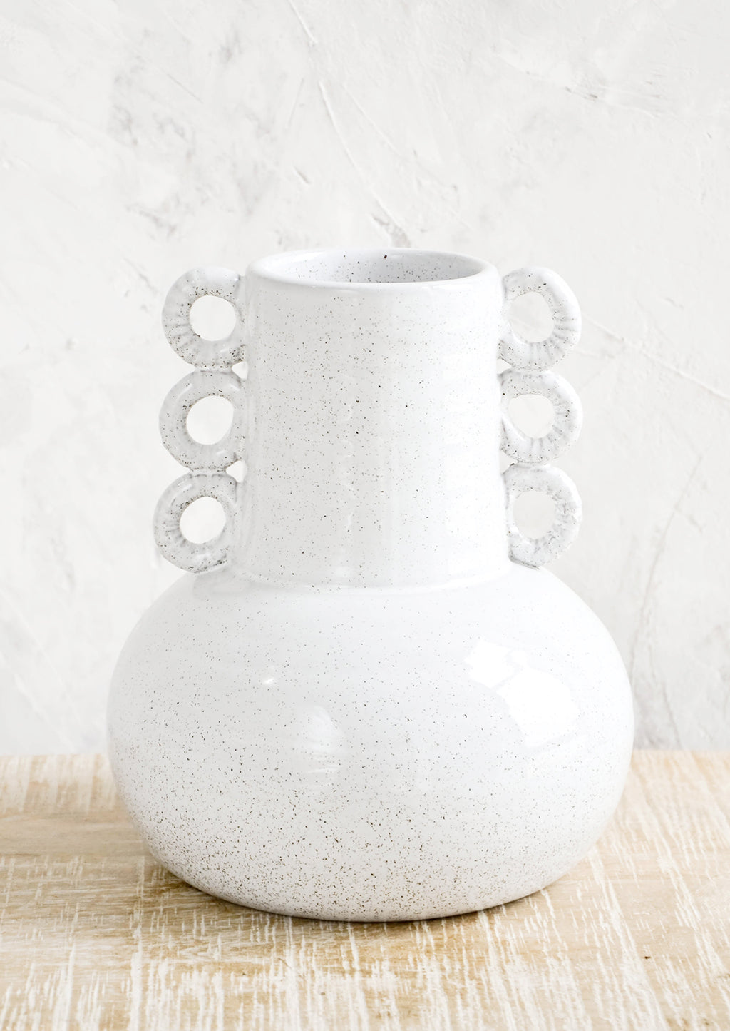 1: Ceramic vase in speckled white glaze. Shape is bulbous at bottom with tapered top and decorative round handles at sides.