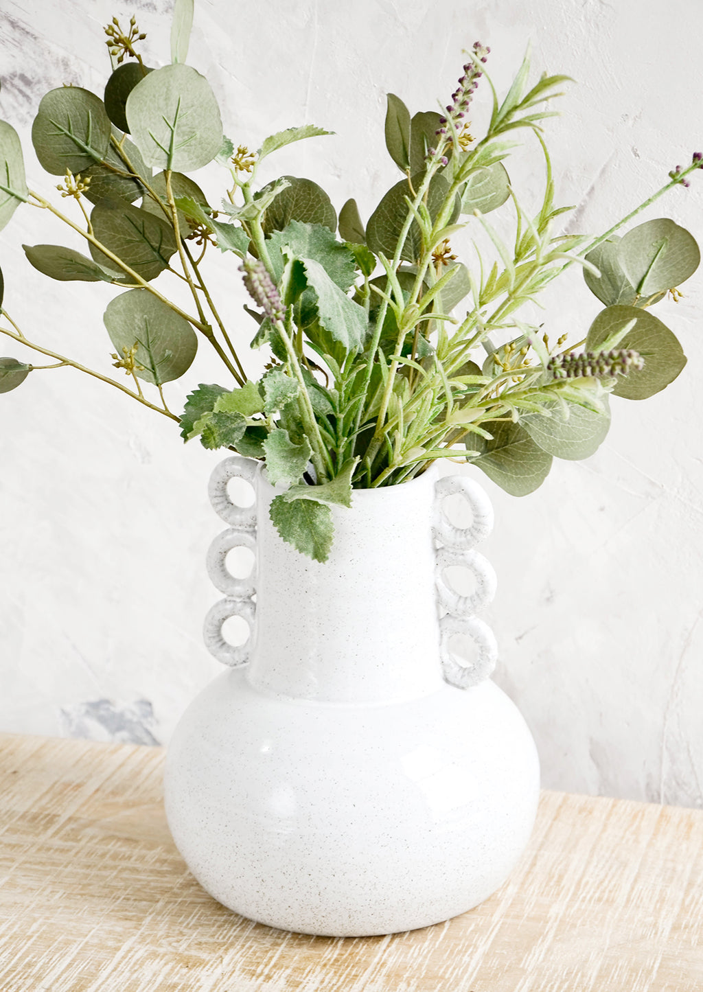 2: Large sculptural white ceramic vase on a rustic table with a mix of herbs & eucalyptus 