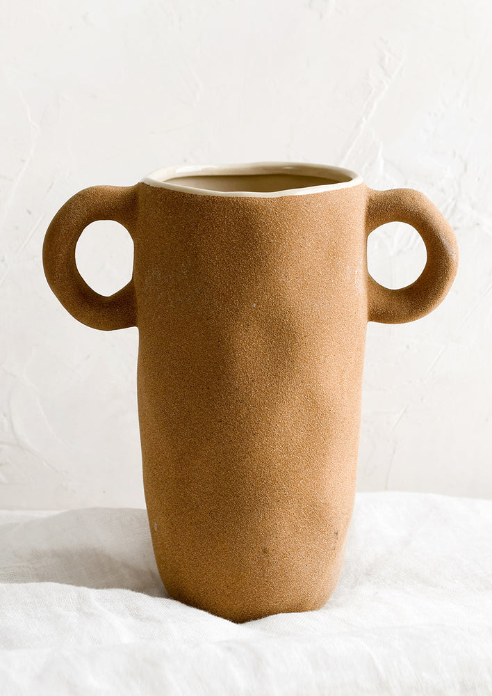 A ceramic vase in tall shape with round side handles at top.