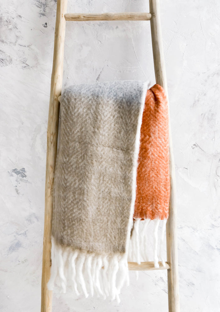 Chunky knit throw blanket in tricolor design with chunky white fringe trim, folded over wooden ladder