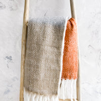 2: Chunky knit throw blanket in tricolor design with chunky white fringe trim, folded over wooden ladder
