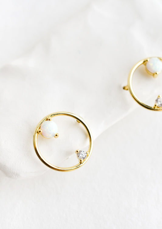 A pair of gold stud earrings in the shape of a circle with opal and crystal detailing.