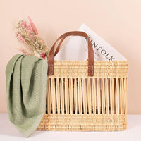 2: A tote-shaped woven reed basket with open air design, brown leather handles.