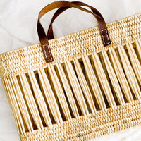 1: A tote-shaped woven reed basket with open air design, brown leather handles.