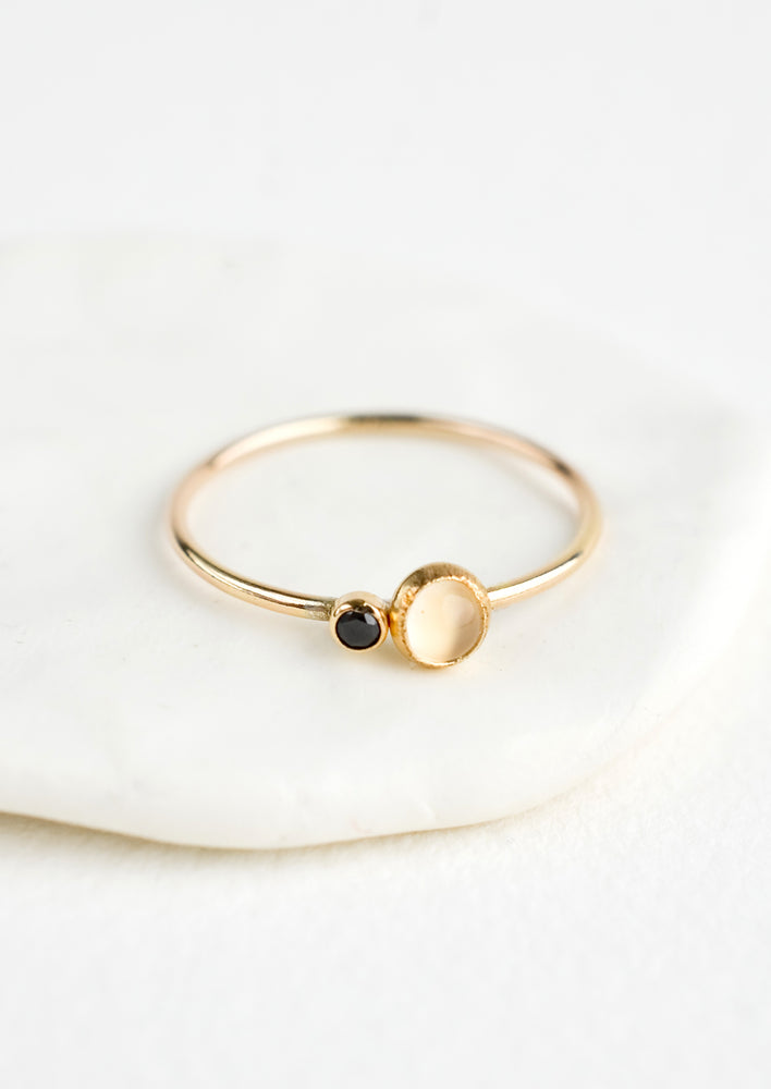 A gold ring with slim band and bezel set moonstone and black CZ.