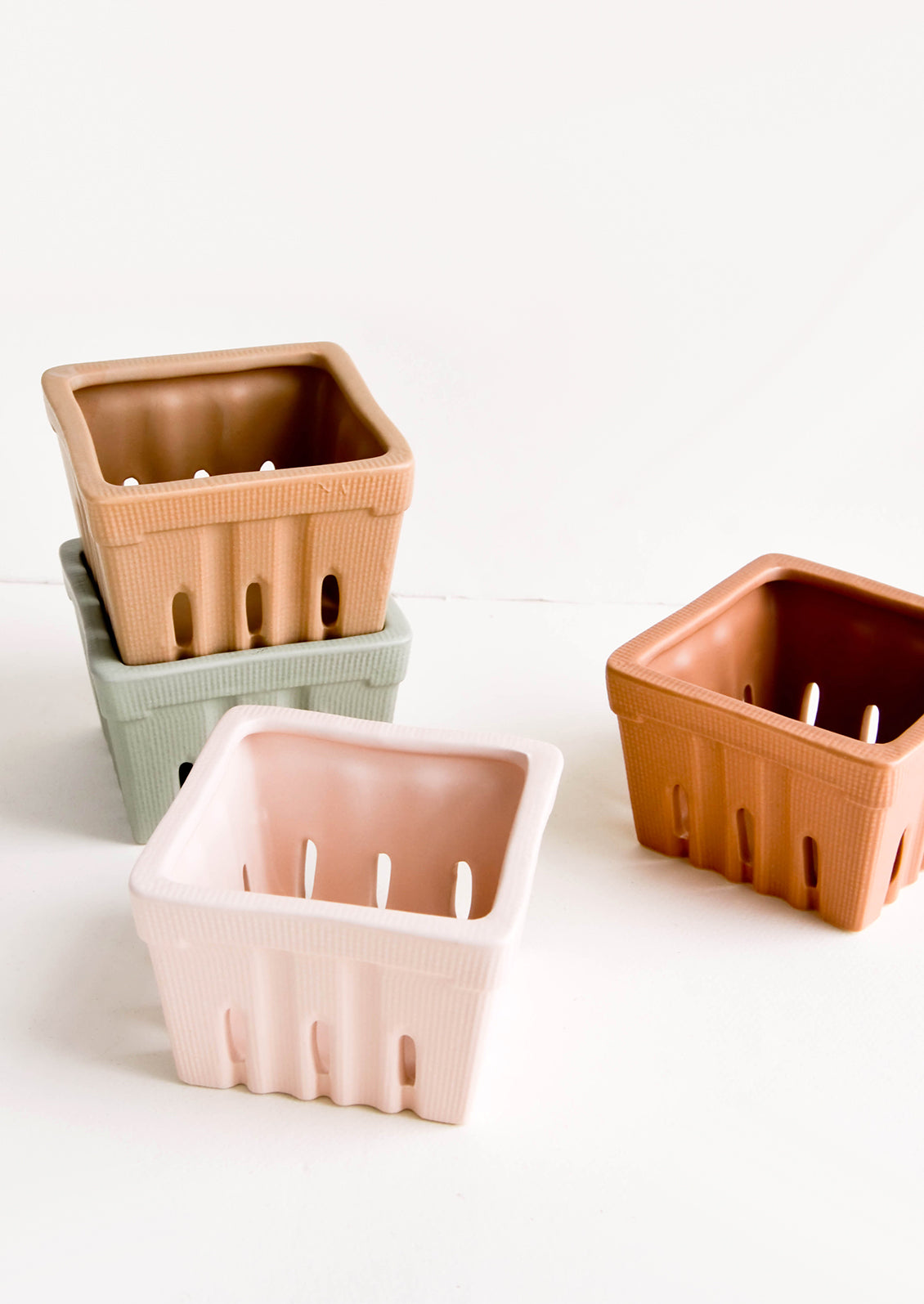 Ceramic baskets in the style of disposable berry baskets, shown in assorted muted hues.
