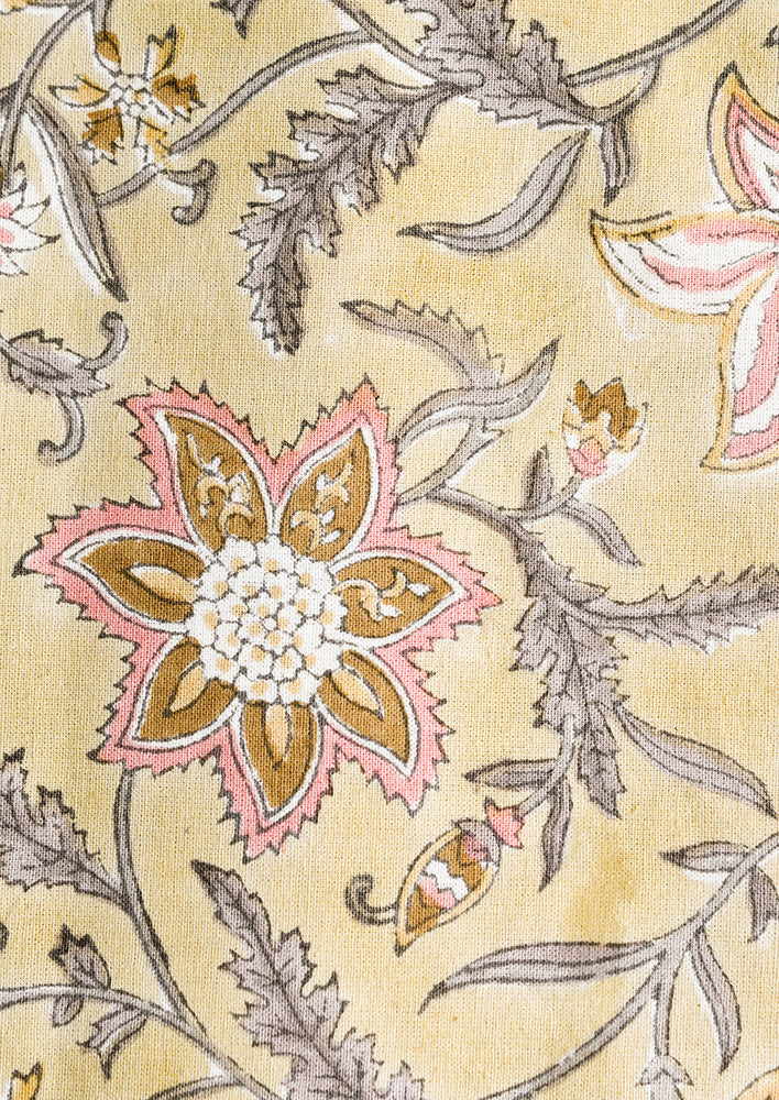 A pale yellow tablecloth with floral print in grey and pink.