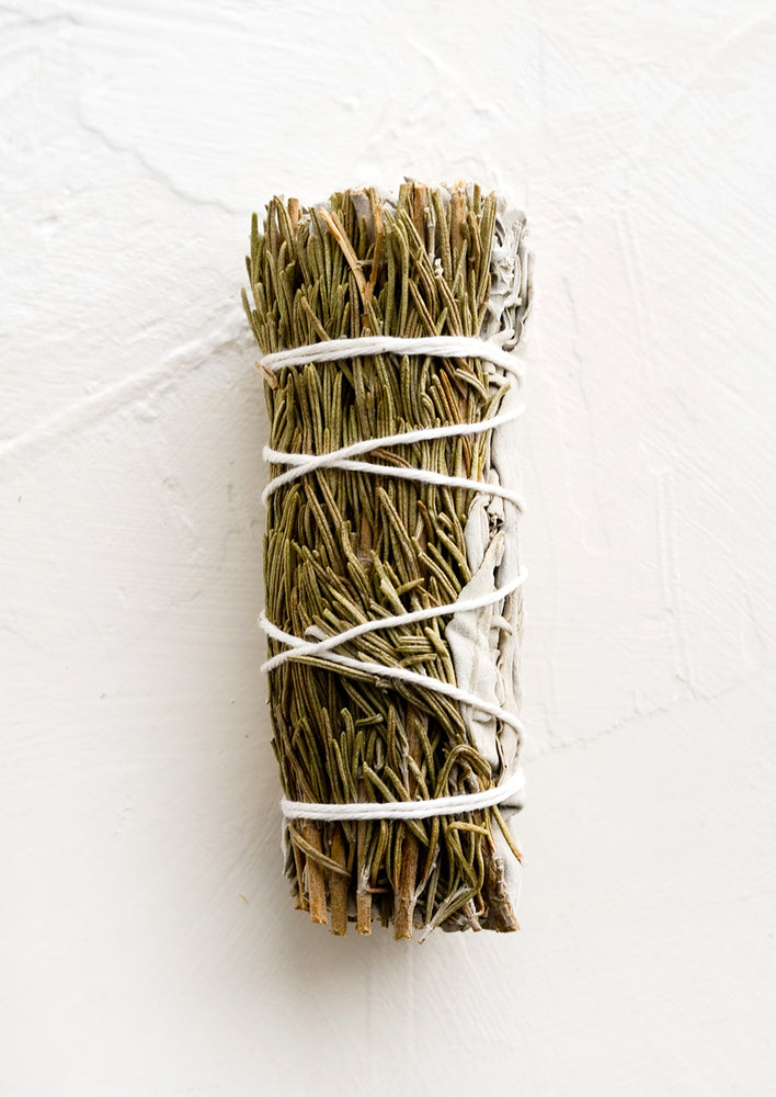 A sage smudge stick wrapped in white thread with rosemary.