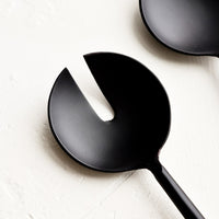 2: A round, matte black metal serving spoon with a slotted notch in the center.