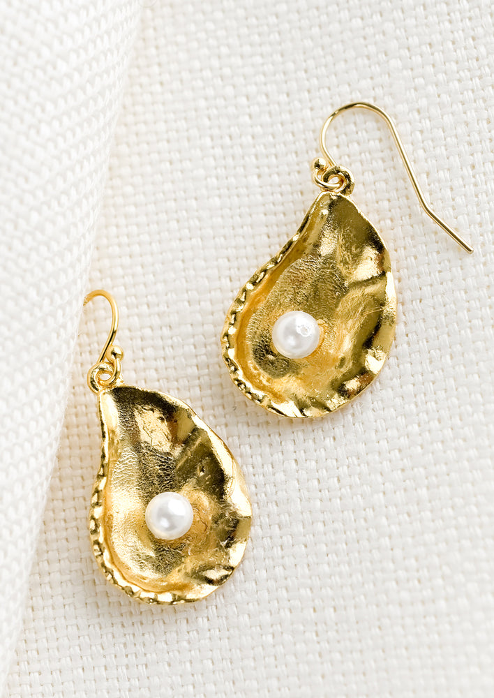 1: A pair of gold oyster shell earrings with single pearl at centers.