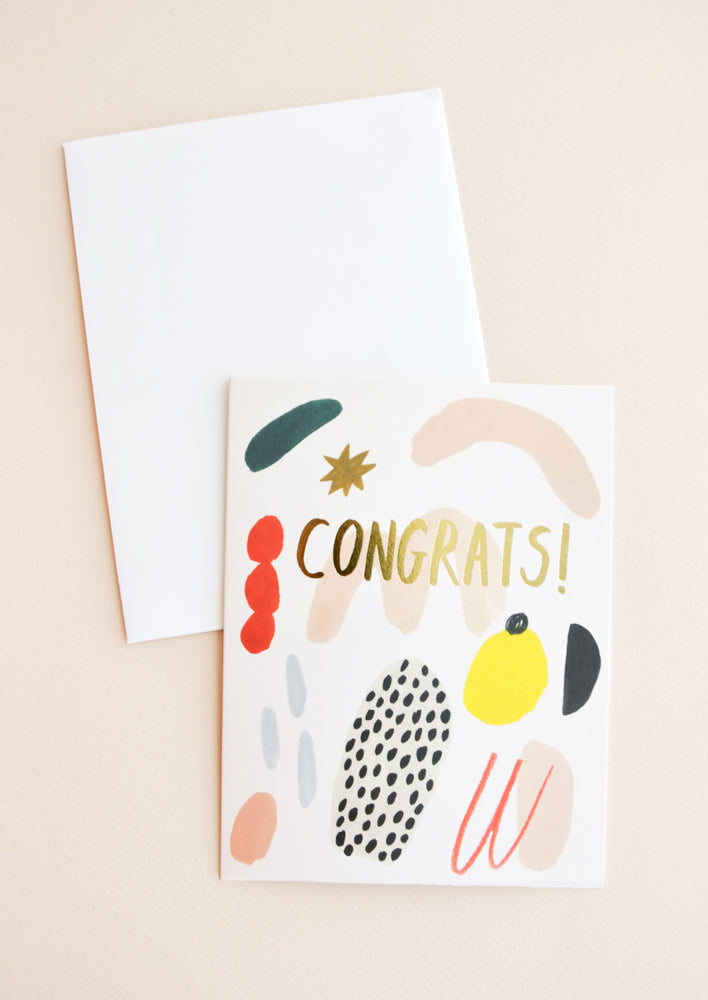 Notecard with colorful abstract shapes and the word "Congrats" in gold, and white envelope.