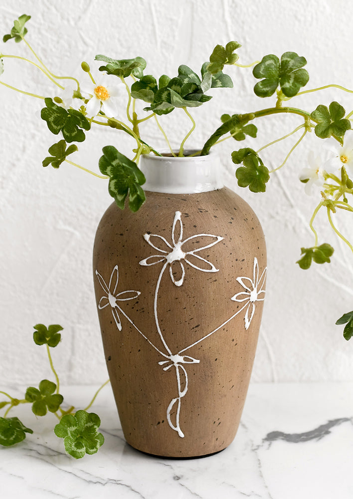 A brown clay vase with white floral sketch.