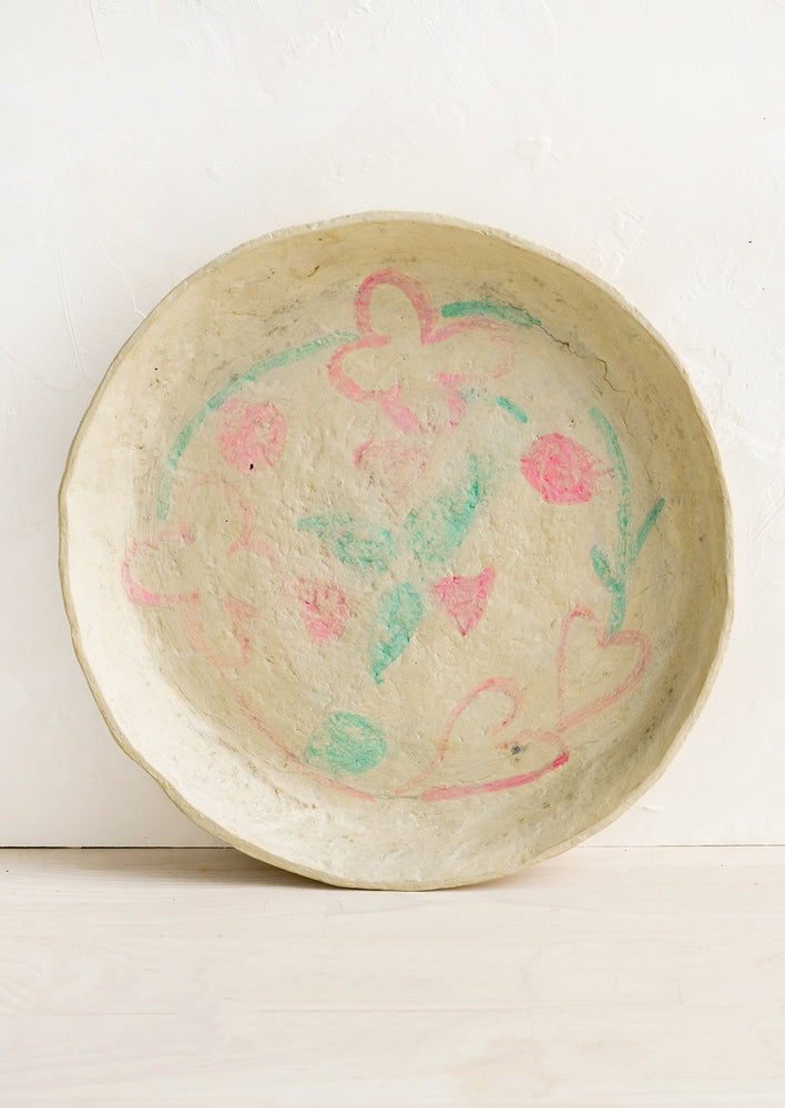 1: A round paper mache tray with faded pink and green design.