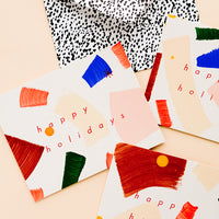 1: Three matching greeting cards with hand-painted brushstrokes and "happy holidays" in red lettering.