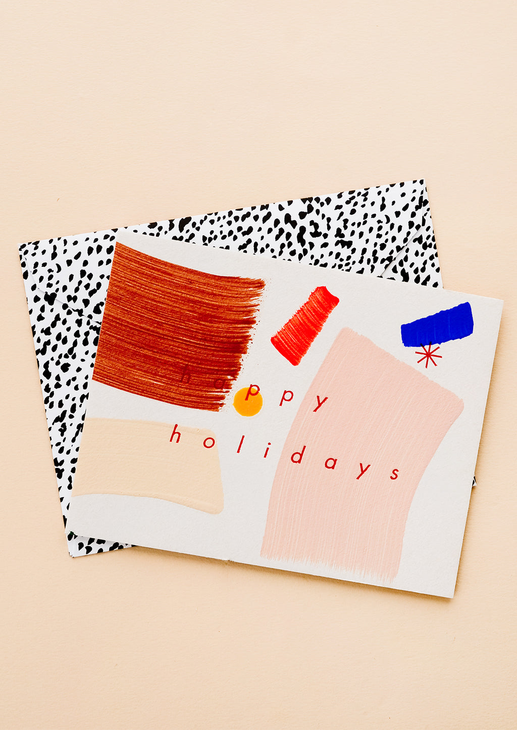 2: A greeting card with hand-painted brushstrokes and "happy holidays" in red lettering, and a black and white patterned envelope.
