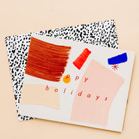 2: A greeting card with hand-painted brushstrokes and "happy holidays" in red lettering, and a black and white patterned envelope.