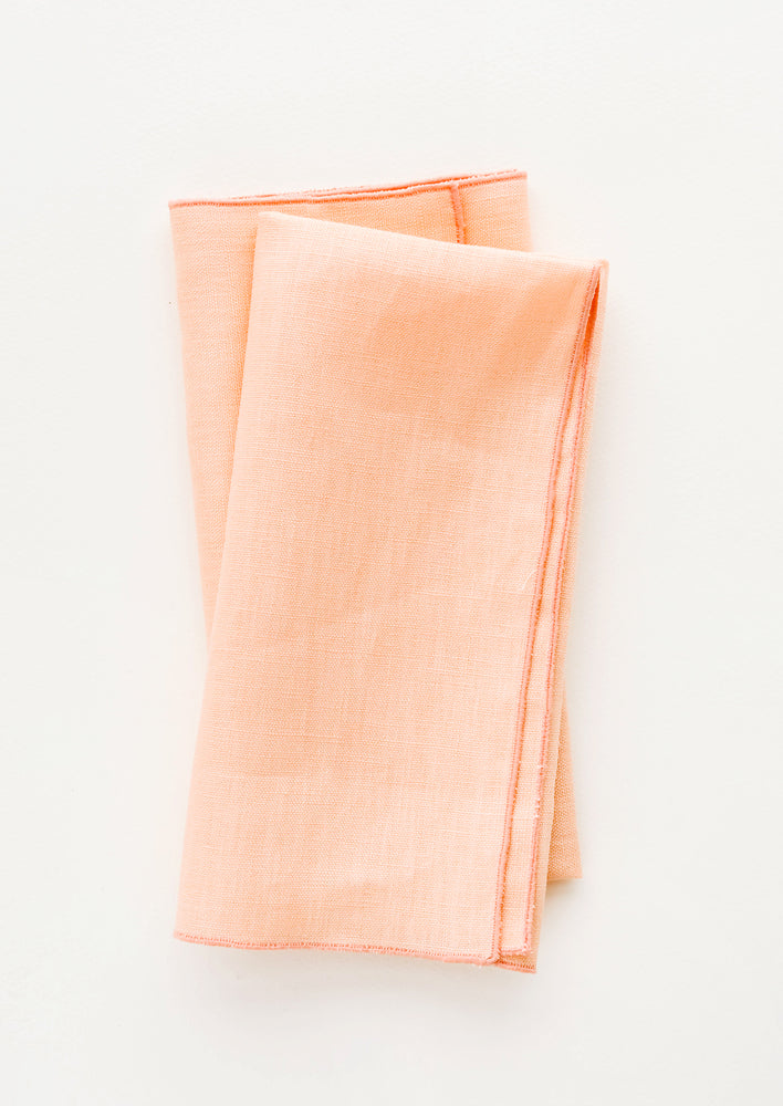 Pair of folded linen napkins in peach with tonal trim