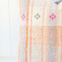 4: A pastel orange and lilac gingham pillow with pink and green embroidery accents.