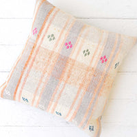 2: A pastel orange and lilac gingham pillow with pink and green embroidery accents.