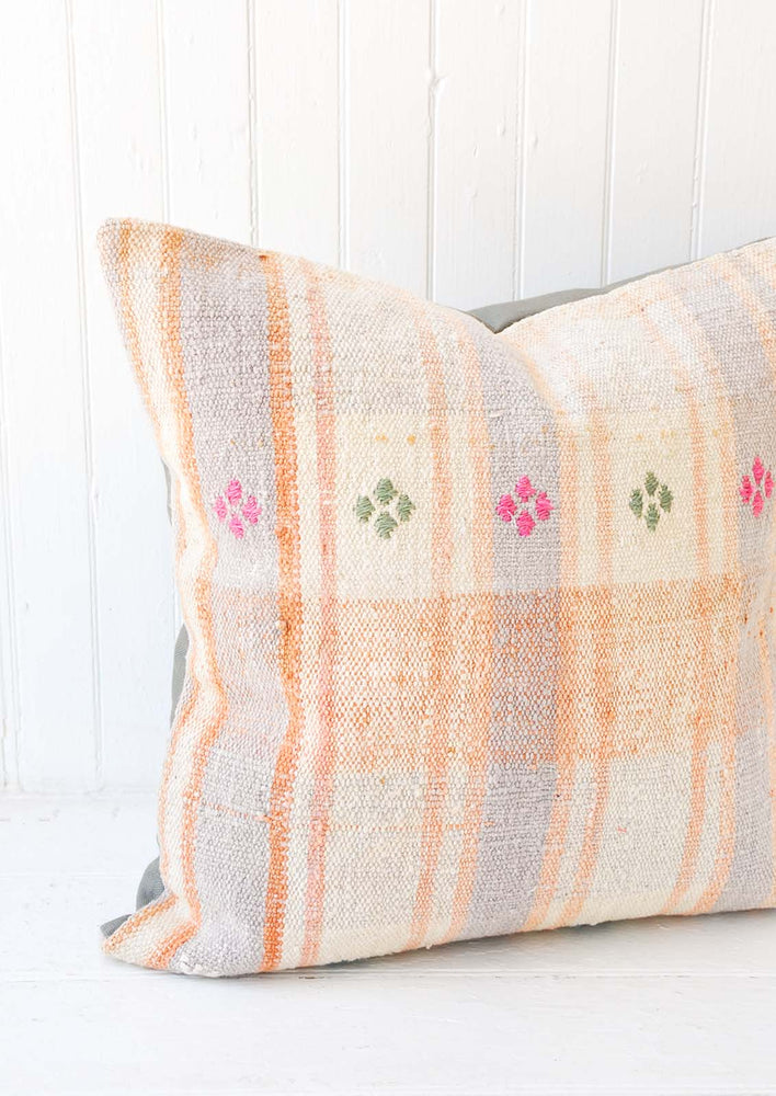 A pastel orange and lilac gingham pillow with pink and green embroidery accents.
