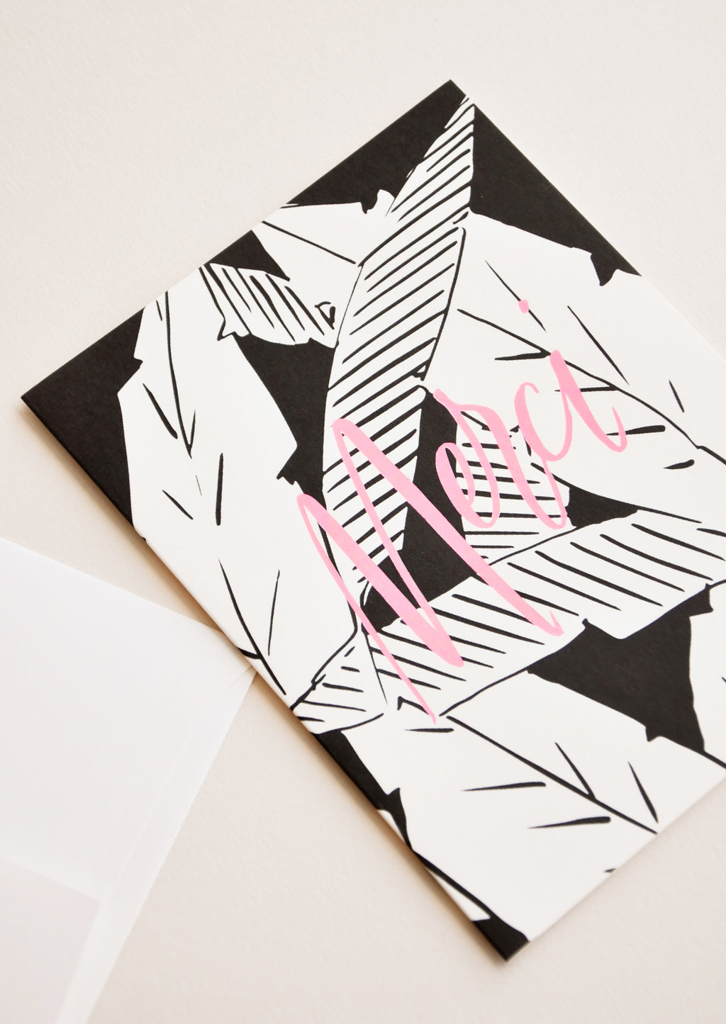2: Notecard with black and white palm leaves decoration and the word "Merci" in pink, and white envelope.