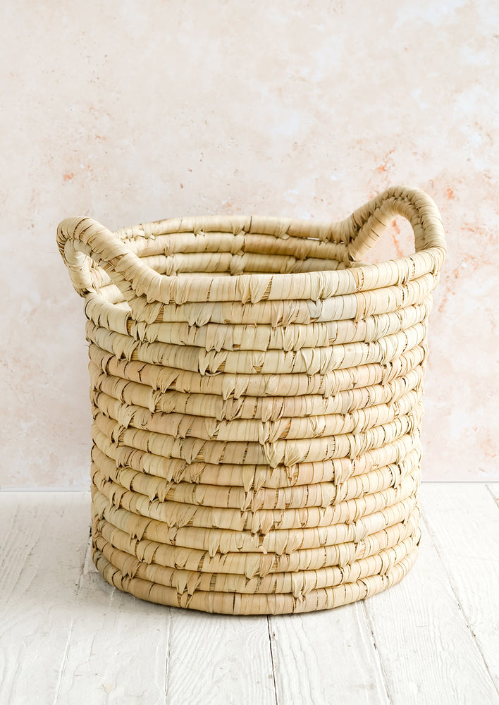 A round, open-top storage bin woven from natural palm leaf