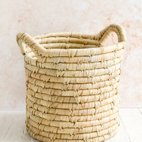 1: A round, open-top storage bin woven from natural palm leaf