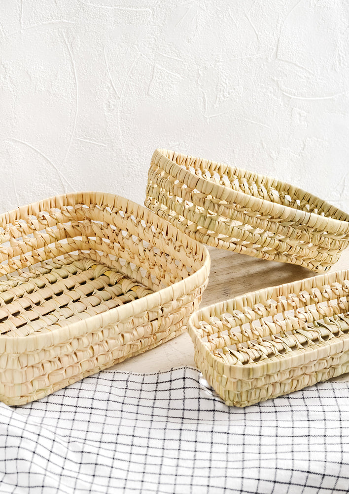 Three shallow baskets woven from natural dried palm leaf.