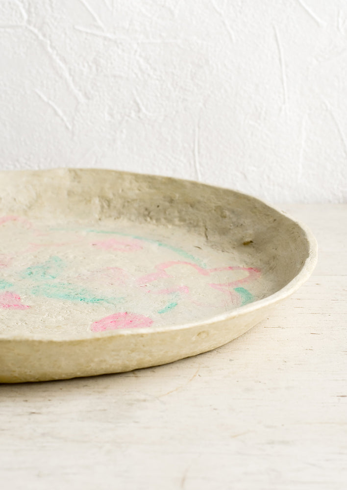 A round paper mache tray with faded pink and green design.
