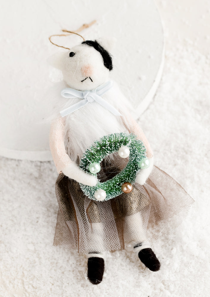 A felted holiday ornament of a cat wearing a dress, holding a wreath.