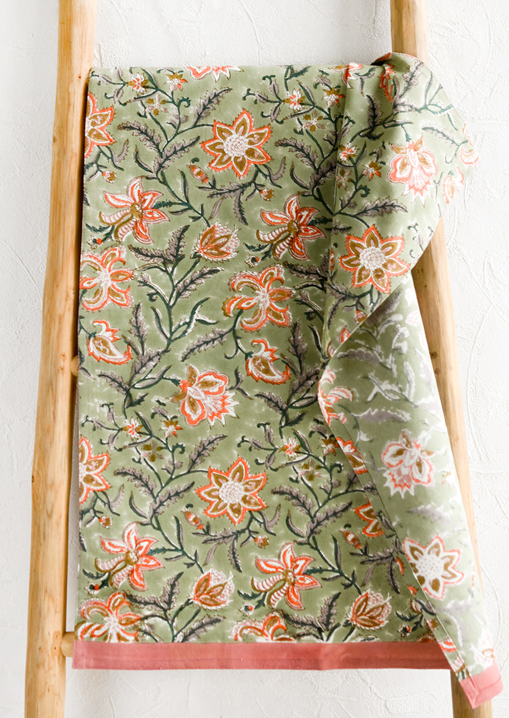 1: A tea towel with sage green background and orange and pink floral print.