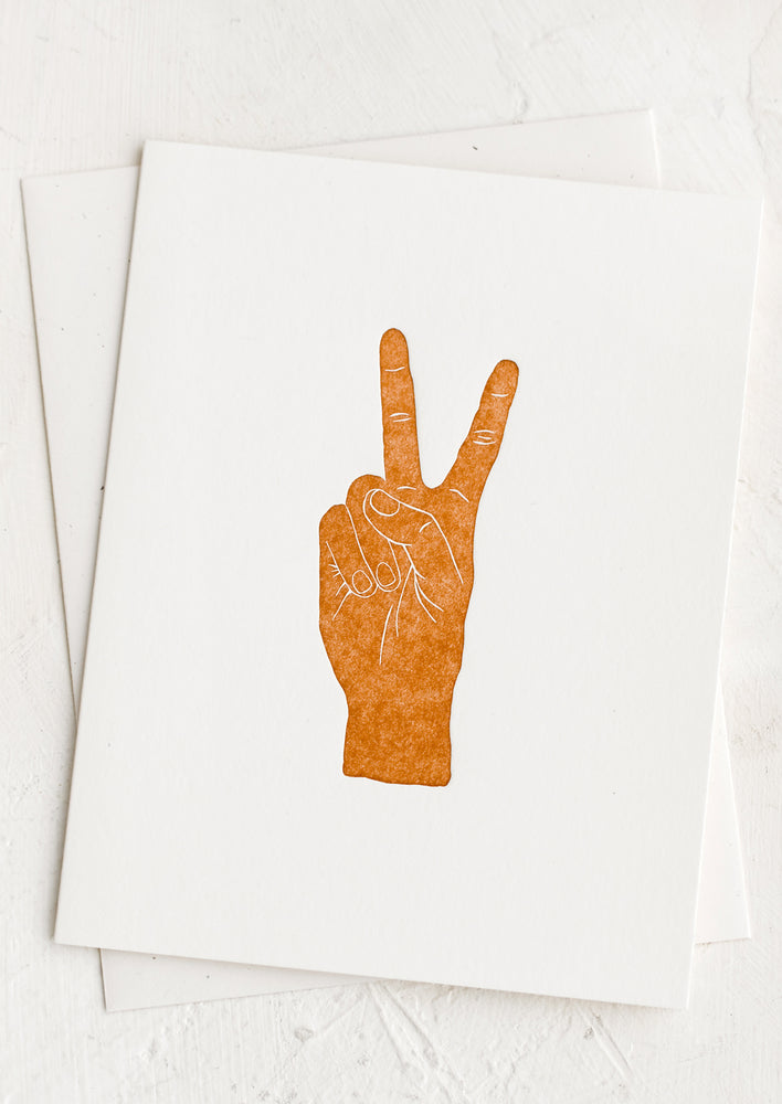 1: A white card with brown letter pressed hand doing a peace sign.