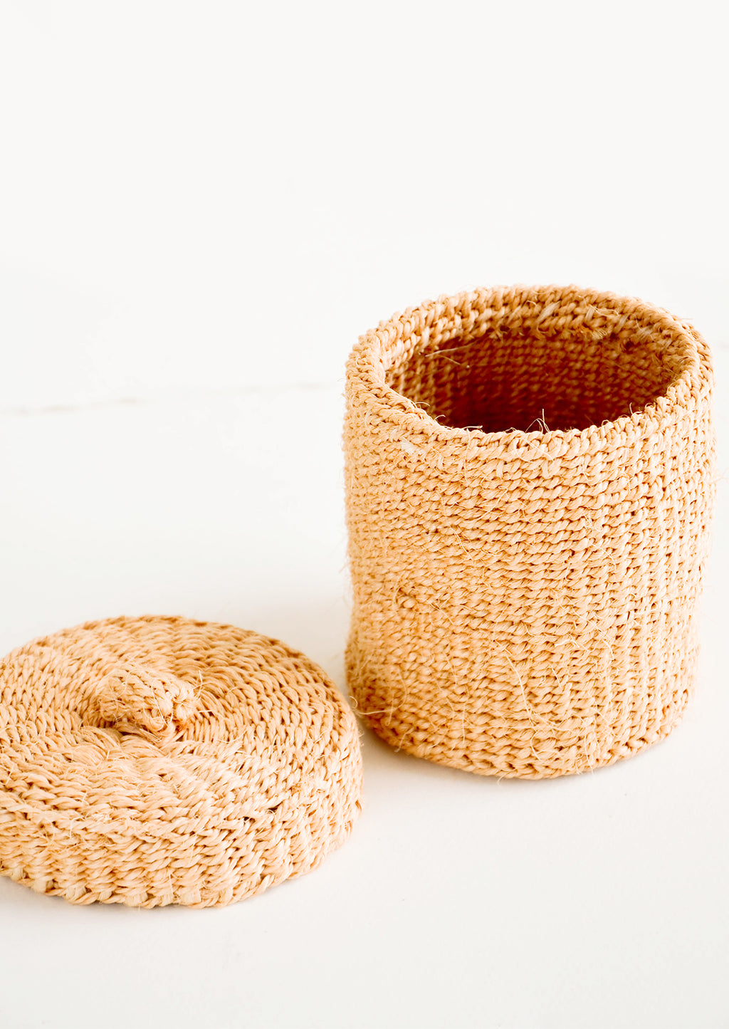 2: Small, round woven basket with matching lid made from peach-colored sisal