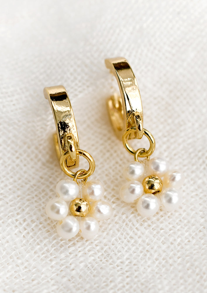 1: A pair of gold huggie hoop earrings with pearl daisy detail.