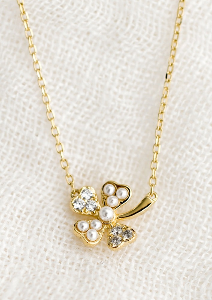 A gold necklace with clover pendant detailed with clear crystals and pearls.