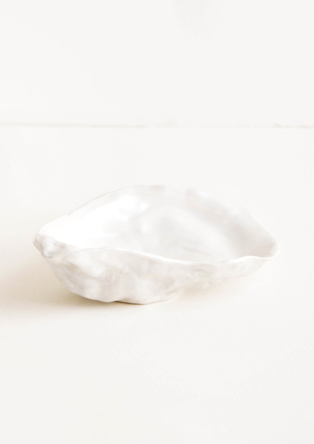 2: A small, pearly white ceramic dish molded in the shape of an oyster half shell