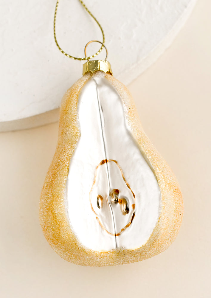 1: A glass holiday ornament of a pear with a slice cut out.